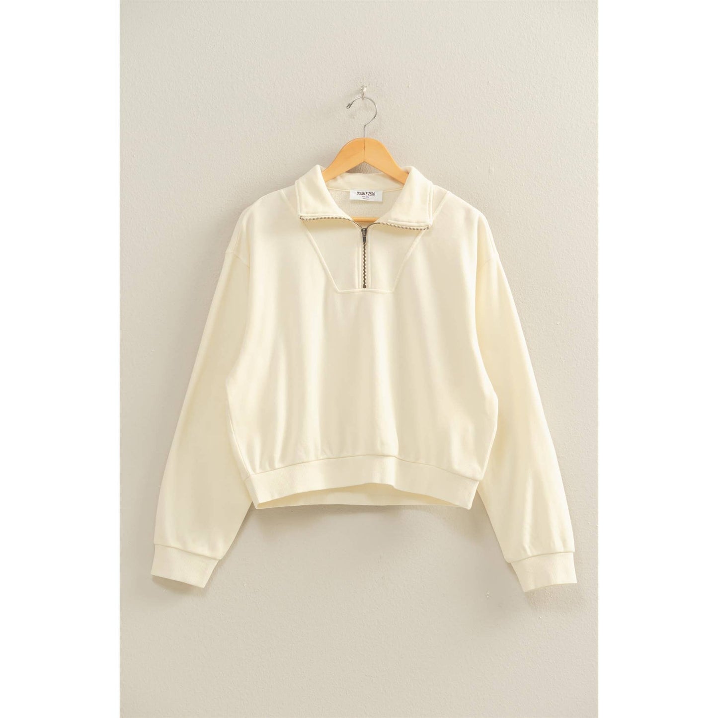 Cream-colored sweatshirt on a wooden hanger against a light gray background