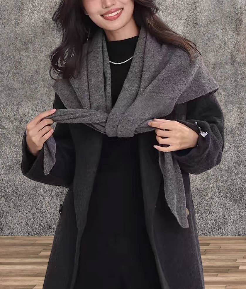 Woman wearing a gray scarf and black coat against a gray textured wall.